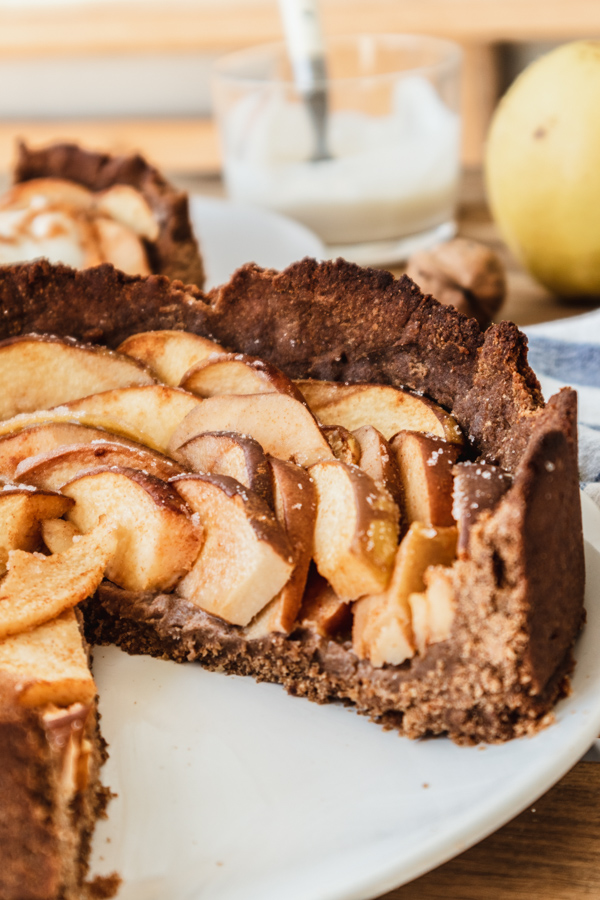 Rezept für einen Quittenkuchen: Der Kuchen ist angeschnitten auf einem Teller. Dahinter ist eine Schale mit Schlagsahne