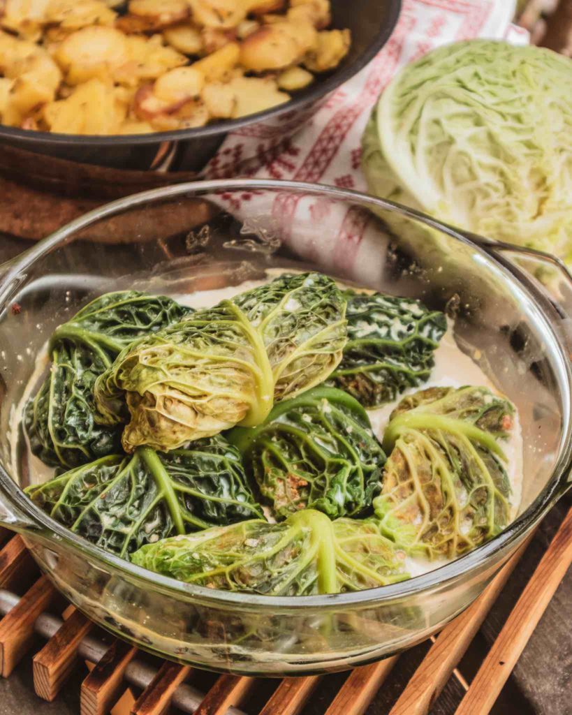 Vegane Wirsing Rouladen werden in einer Auflaufform gebraten. Dazu passen krosse Bratkartoffeln.